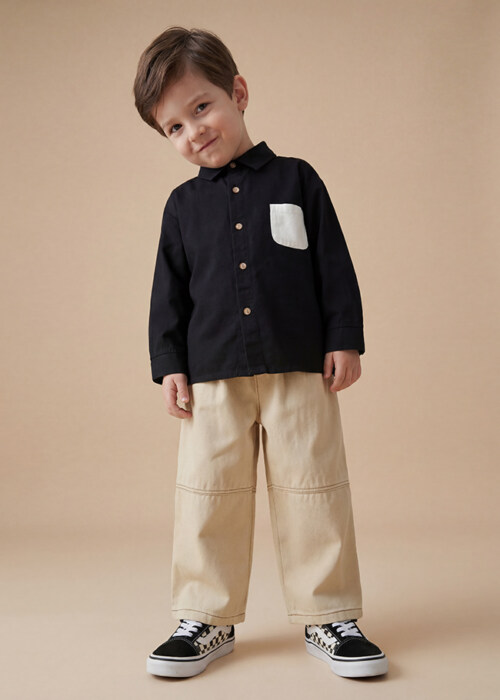 AI model photography of a black button-up kids shirt with contrast pocket and beige pants, front view on a tan background