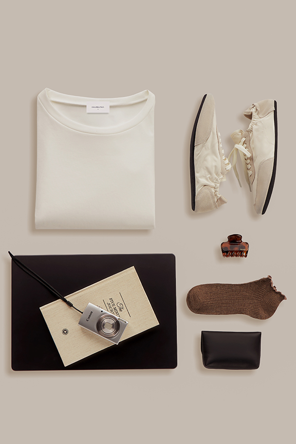 Creative flat lay clothing photography for ecommerce. Folded white tee, ivory sneakers and accessories on a beige background.