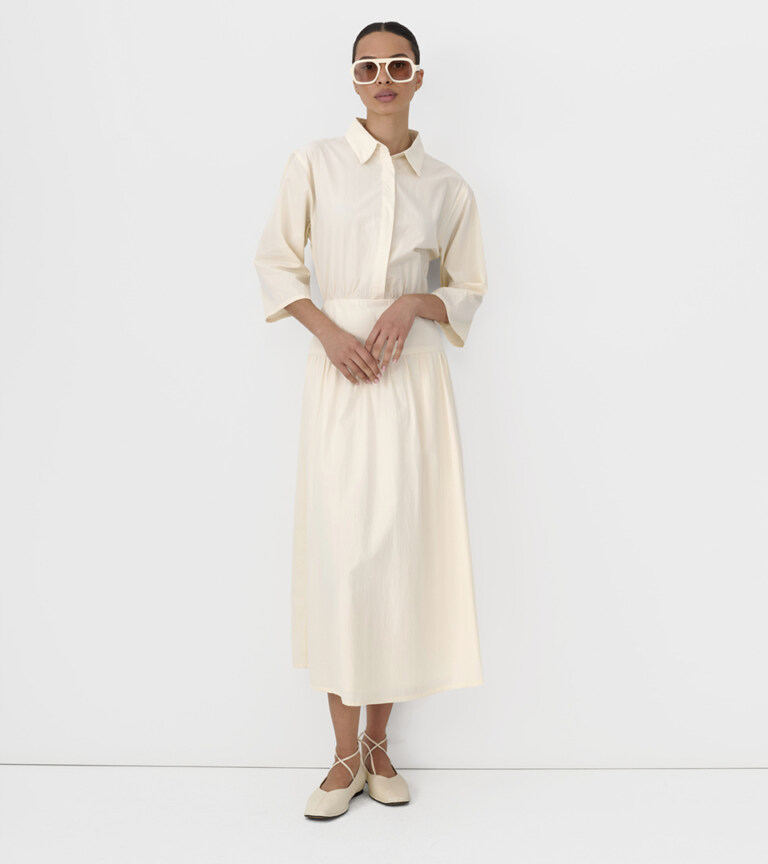 fashion model in cream shirtdress wearing white sunglasses on light grey studio background