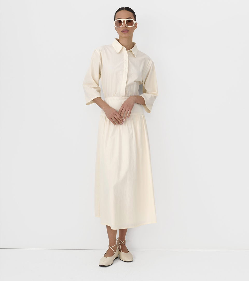 fashion model in cream shirtdress wearing white sunglasses on light grey studio background