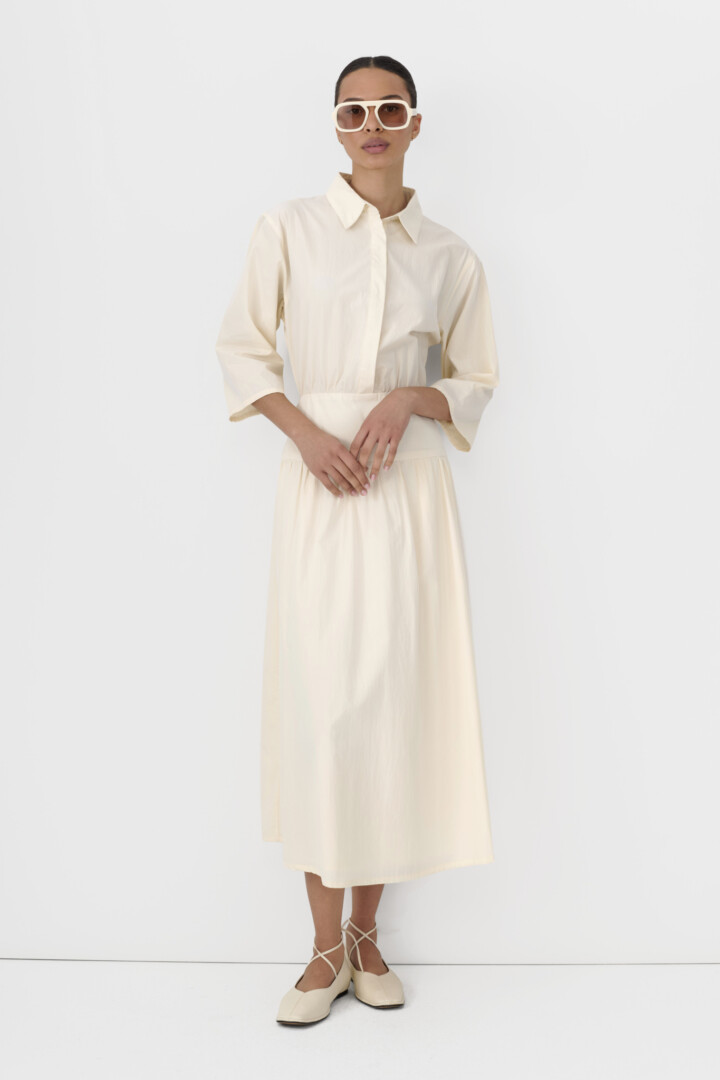 Ecommerce product photography and video production studio. Model in cream collared shirt dress with white square sunglasses on white.