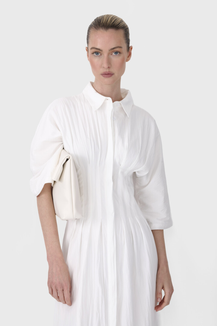 Fashion ecommerce reels and product video production. Close-up of model in white pleated shirt dress holding an ivory clutch.