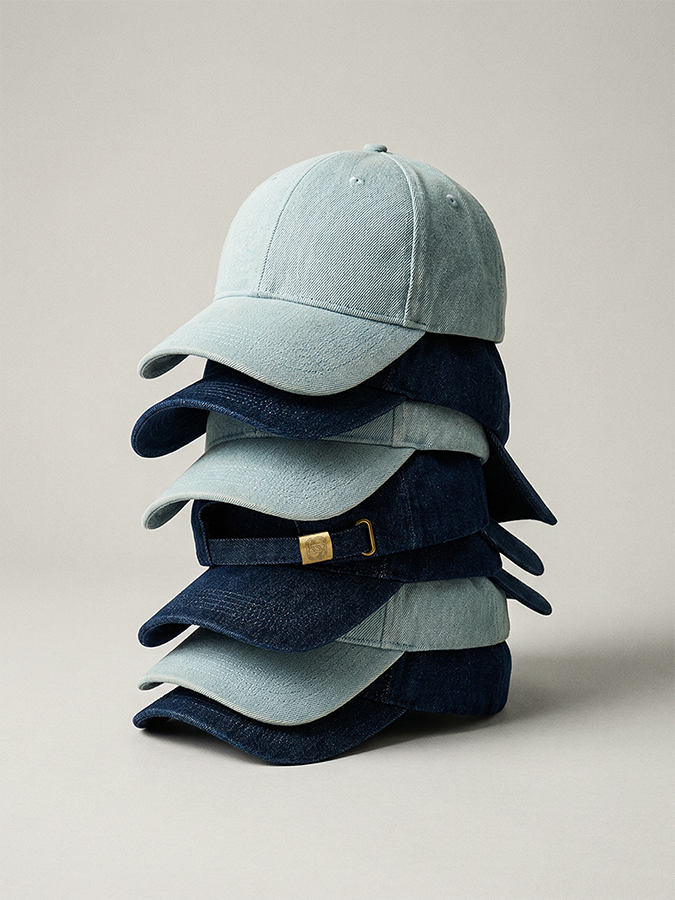 Product photography studio all-in-one for clothing brands. Stack of denim baseball caps in graduated blue shades on a beige background.
