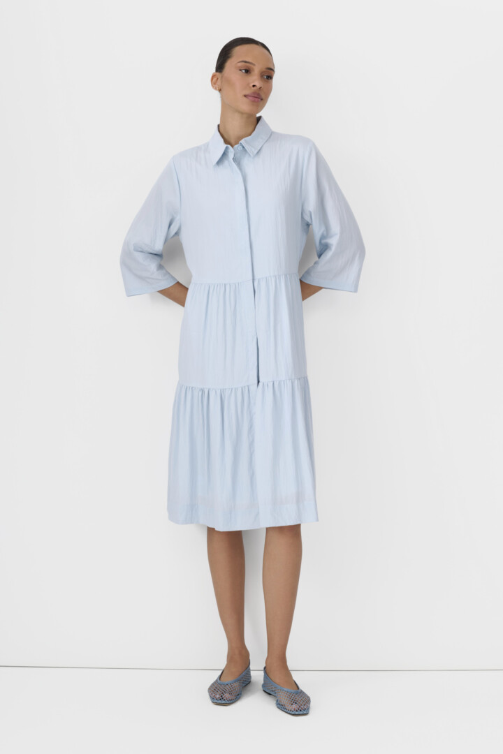 Social media content product photography studio by Shootify. Model in light blue tiered shirt dress with blue mesh flats on white.