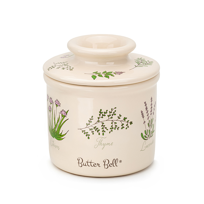 Product photography of a ceramic butter crock with botanical herb illustration, lid closed, on a white background