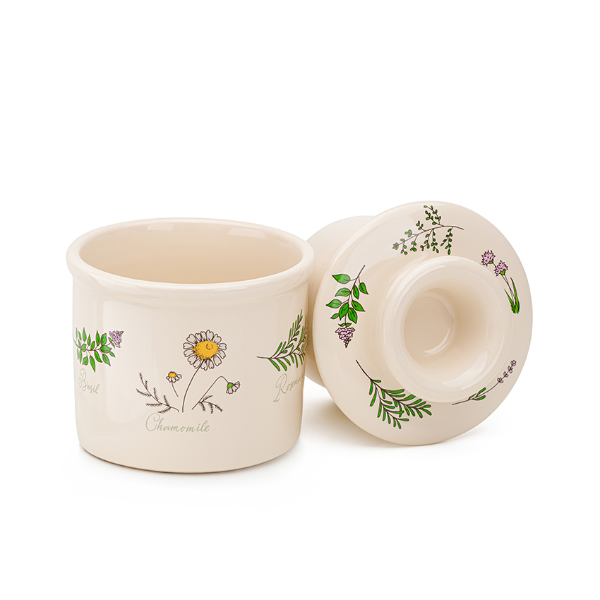 Product photography of a ceramic butter crock with daisy pattern, bell lid tipped on its side showing the interior
