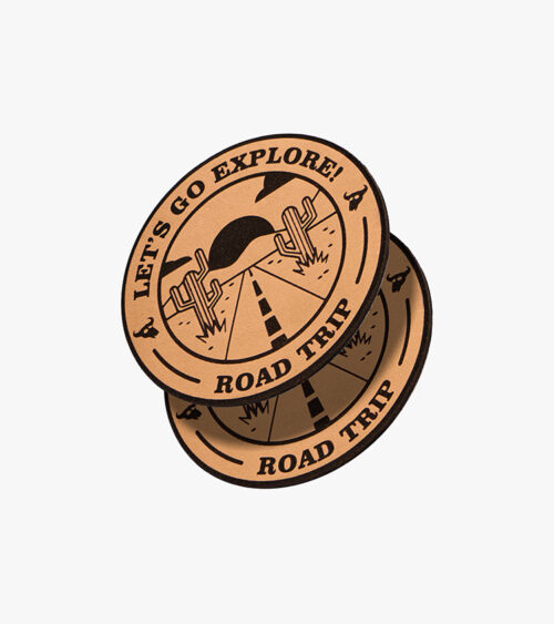 Product photography of two engraved leather patches with a road-trip design, stacked at an angle on a light background.