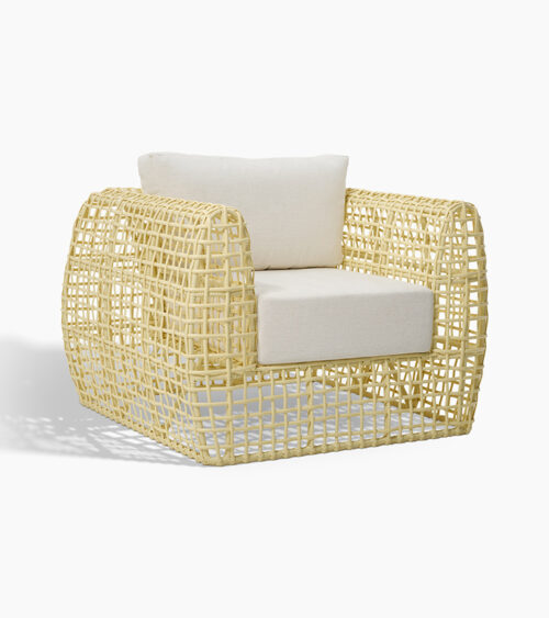 Furniture product photography of an open-weave rattan lounge chair with white cushions, three-quarter view.