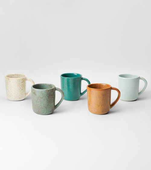Product photography of a five-piece ceramic mug collection in speckled glazes, grouped on a seamless background.