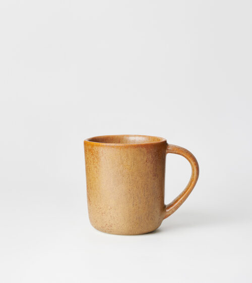 Studio product photography of a speckled ochre ceramic mug, side view on a light seamless background.