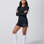 Female model in black long sleeve adidas top with white shorts and socks