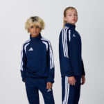 Two teen models in matching navy adidas tracksuits, side view
