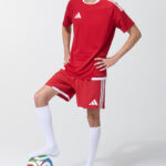 Male model in red soccer jersey and shorts with foot resting on a soccer ball