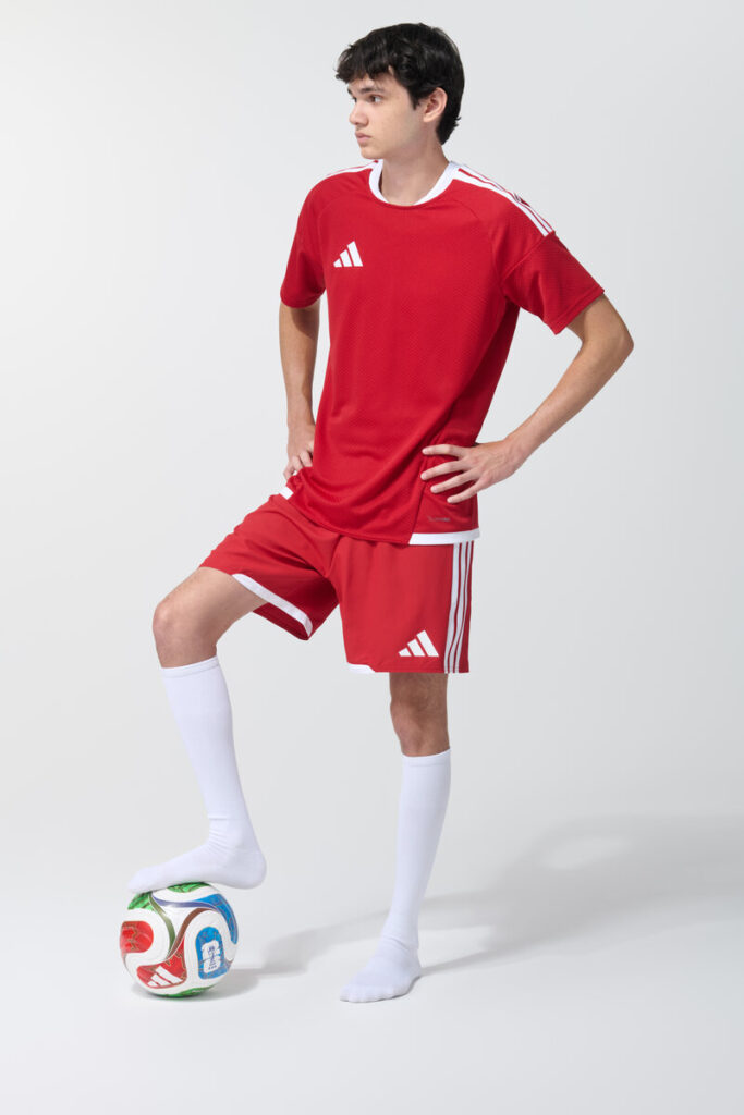 Male model in red soccer jersey and shorts with foot resting on a soccer ball