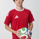 Male model in red adidas soccer jersey holding a soccer ball