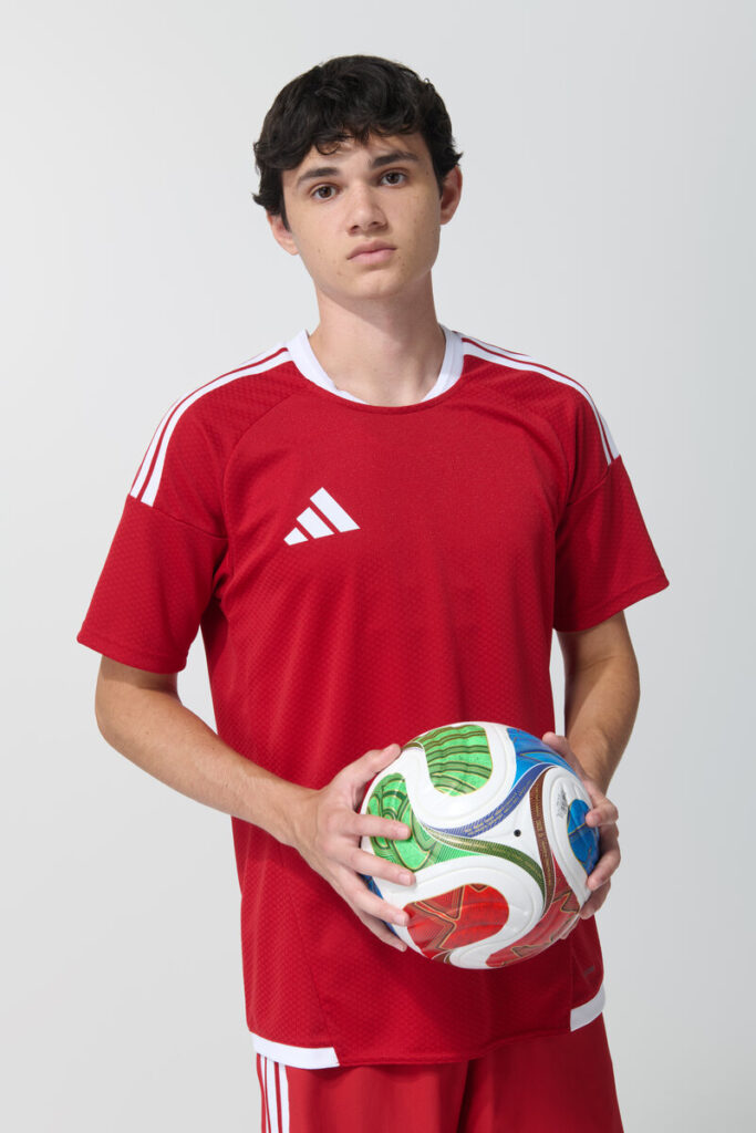 Male model in red adidas soccer jersey holding a soccer ball