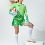 Female model in neon green goalkeeper jersey holding a soccer ball