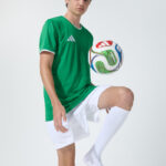 Male model in green soccer jersey balancing a soccer ball on his foot