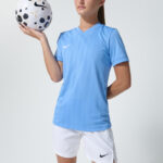 Female model in light blue soccer jersey holding a soccer ball