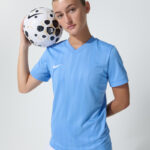 Male model in light blue soccer jersey holding a soccer ball on his shoulder
