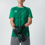 Male model in green soccer jersey and grey shorts wearing goalkeeper gloves