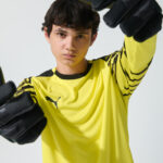 Male model in yellow goalkeeper kit in action pose with gloves raised