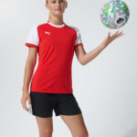 Female model in red Puma soccer jersey holding a soccer ball