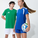 Two youth models in green and blue soccer jerseys holding a soccer ball together
