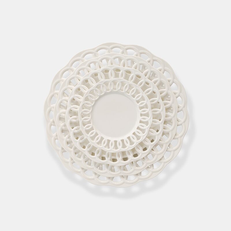 Product photography of four white ceramic plates with open lattice rims, stacked by size and shot from above