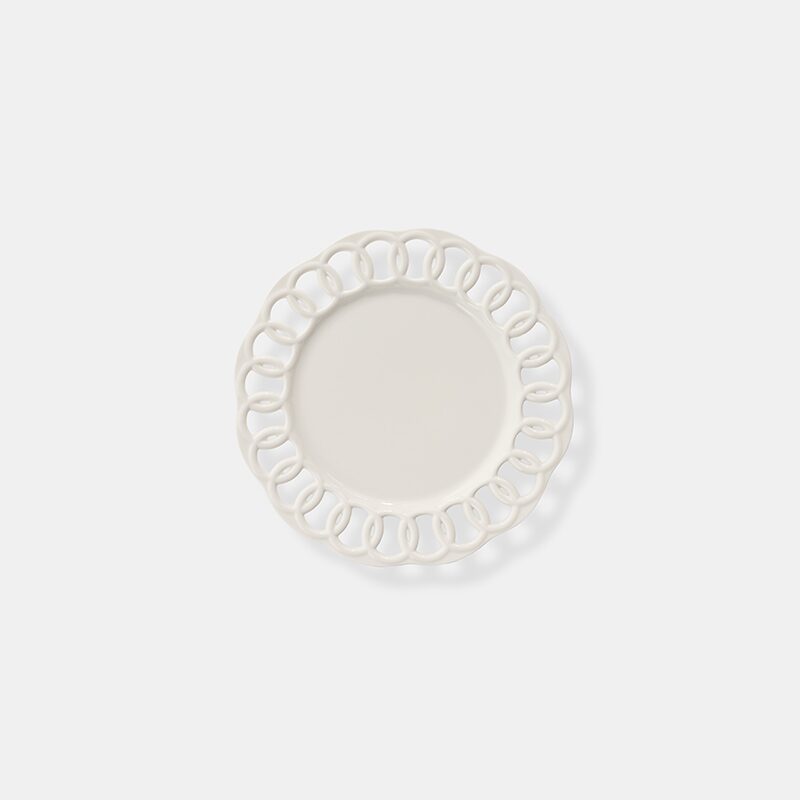 Product photography of a white ceramic side plate with an open lattice rim, shot from above on white