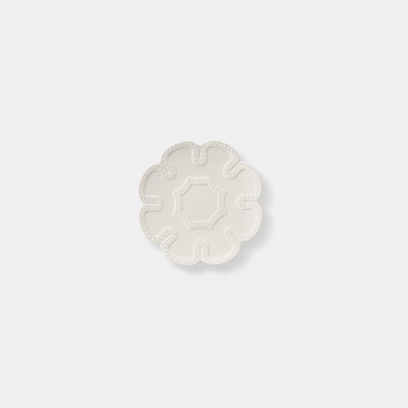 Product photography of a small white ceramic plate with a scalloped flower-shaped rim and beaded detail, shot from above