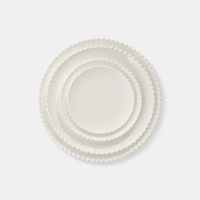 Product photography of four white ceramic plates with scalloped rims, nested by size and shot from above