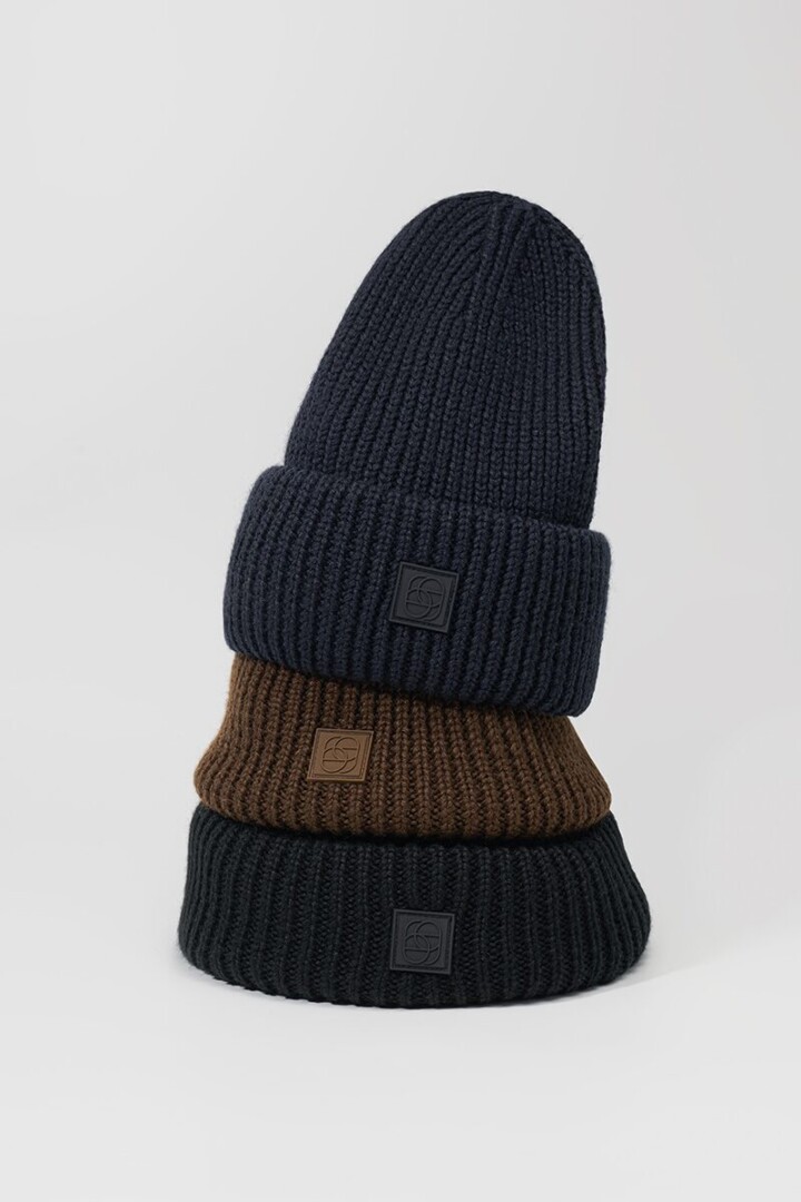 Product photography of three ribbed knit beanies in navy, brown and black stacked on an off-white background with a soft natural shadow