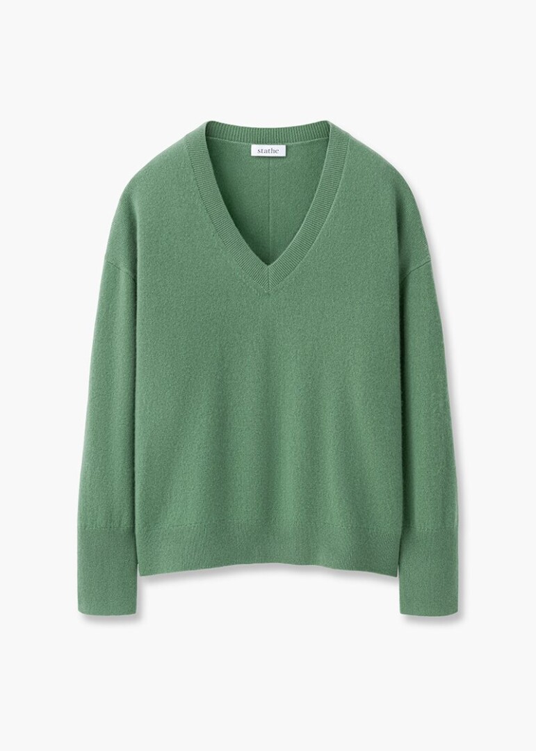 Flat lay product photography of a green V-neck cashmere sweater with dropped shoulders, front view on white
