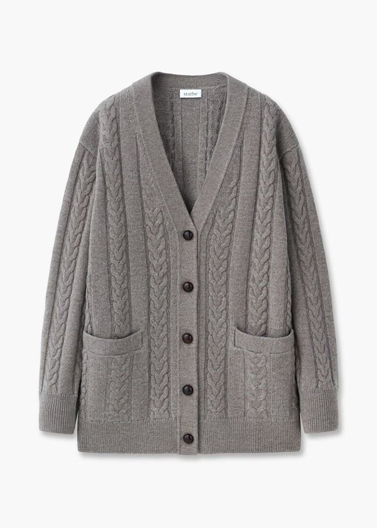 Shaped flat lay product photography of a grey cable-knit cardigan with patch pockets and horn buttons, front view on white