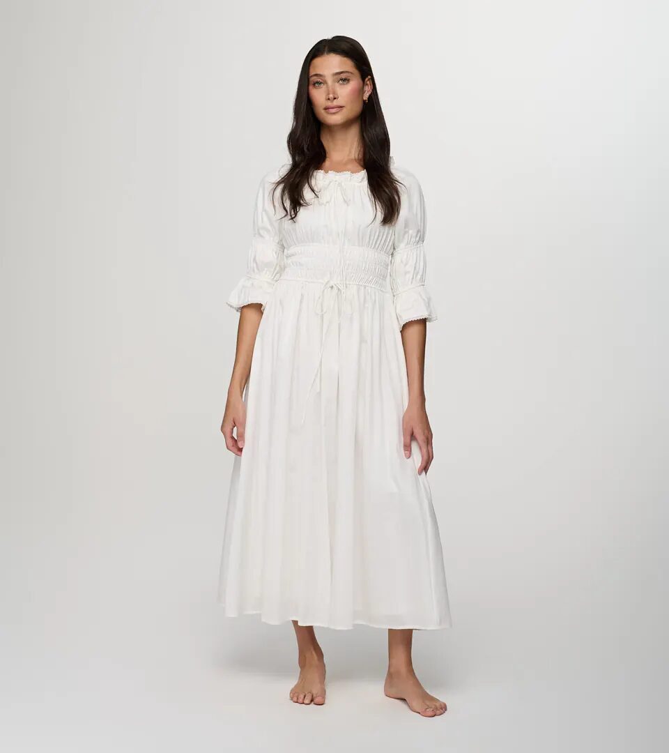 On-model photography of a white cotton midi dress with a smocked waist, ruffled sleeves and a tie belt, full-length front view