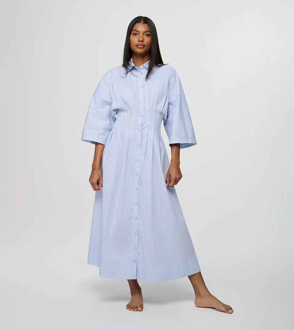 On-model photography of a blue and white striped cotton shirt dress with wide sleeves and a fitted waist, full-length front view