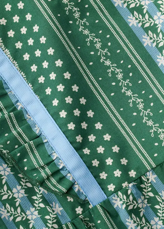 Fabric swatch close-up of a green and white floral stripe print with a blue grosgrain ribbon trim and ruffle seam
