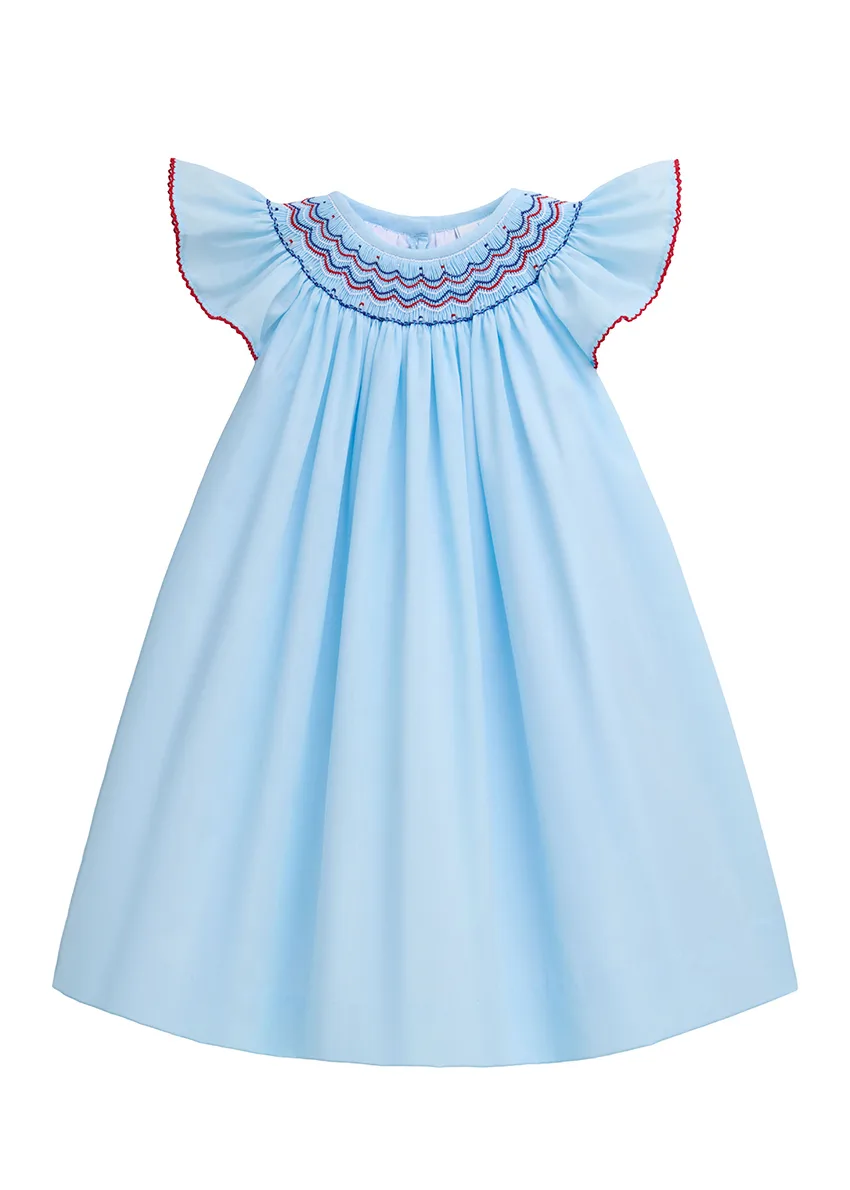 Light blue bishop dress with red and blue smocked yoke and flutter sleeves, photographed as a styled flat lay on white
