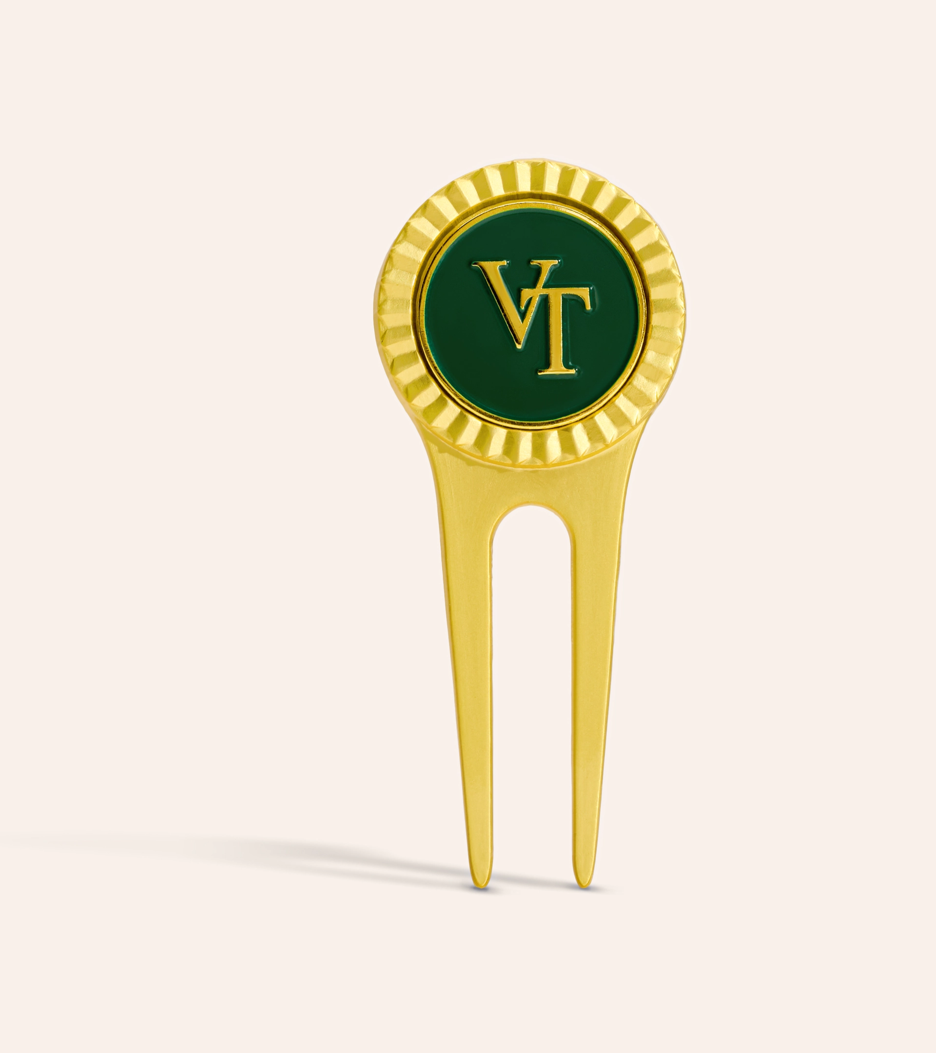 Accessory photography of a gold golf divot tool with a green enamel monogram