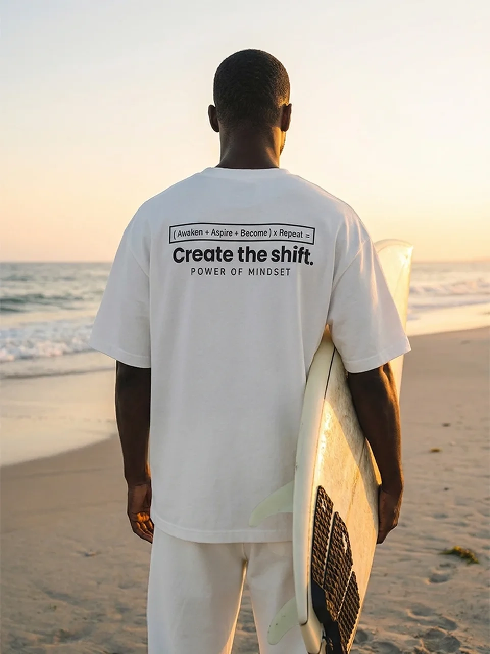 AI model photography of a man on a beach holding a surfboard, wearing a white printed T-shirt, back view