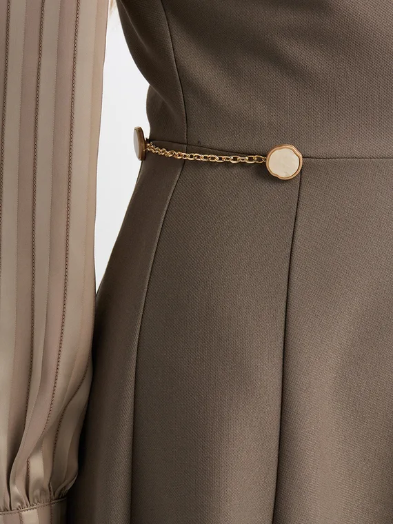 Close-up of the gold chain and button trim at the waist of a taupe dress