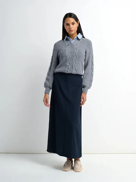 Model in a grey cable knit sweater layered over a blue striped shirt with a navy skirt