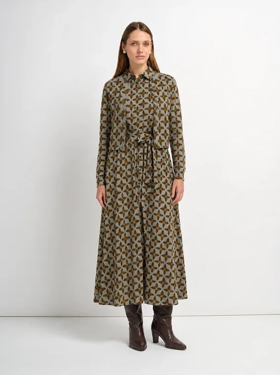 Model in an olive and gold geometric print shirt and matching midi skirt with brown boots