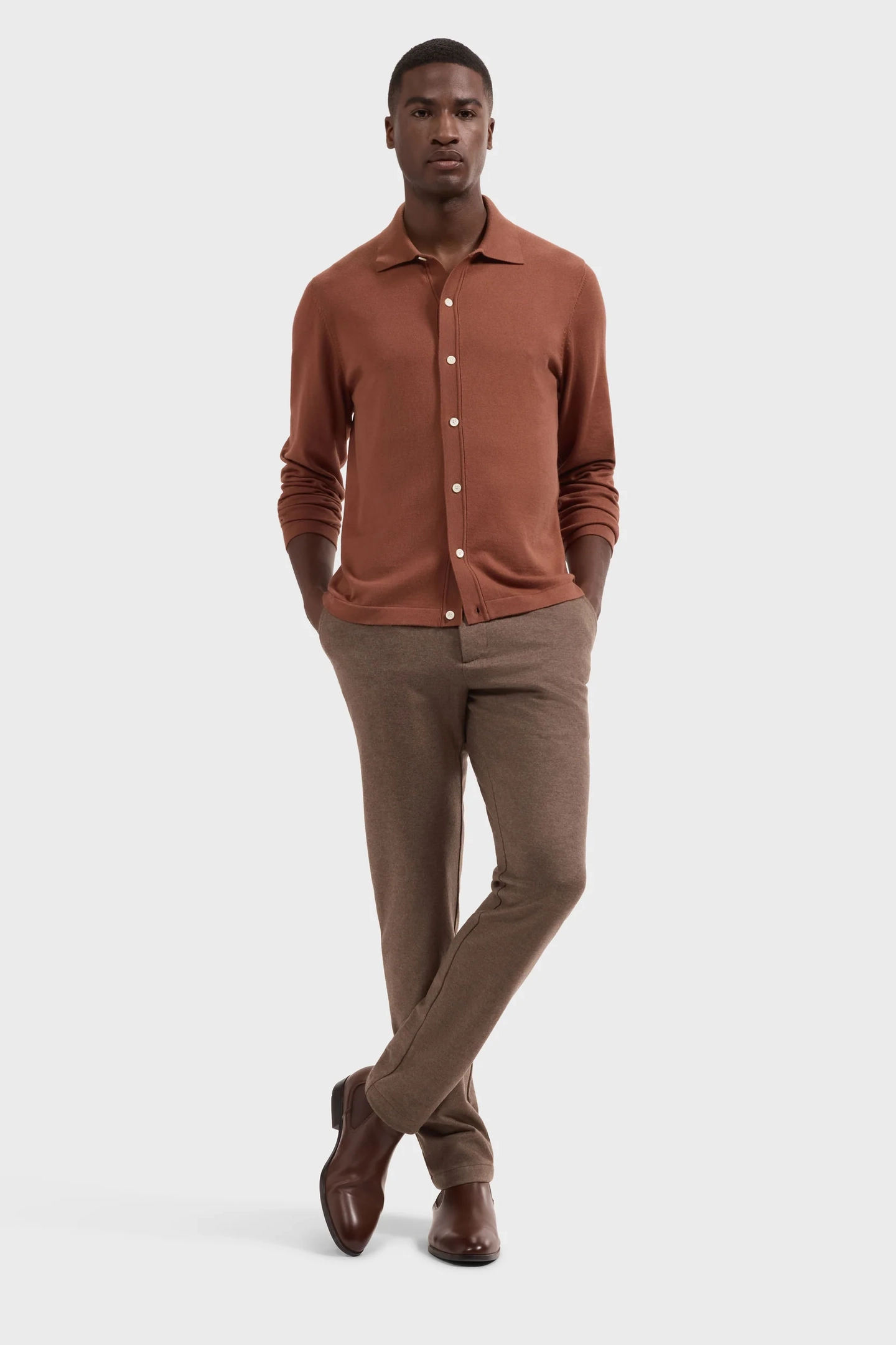 On-model photography of a rust knit button-up shirt and brown trousers