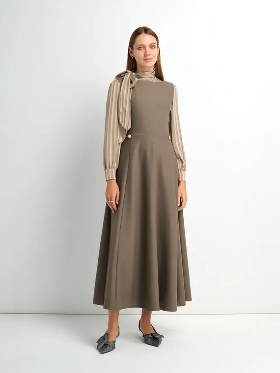 Model in a taupe sleeveless dress worn over a striped scarf-tie blouse