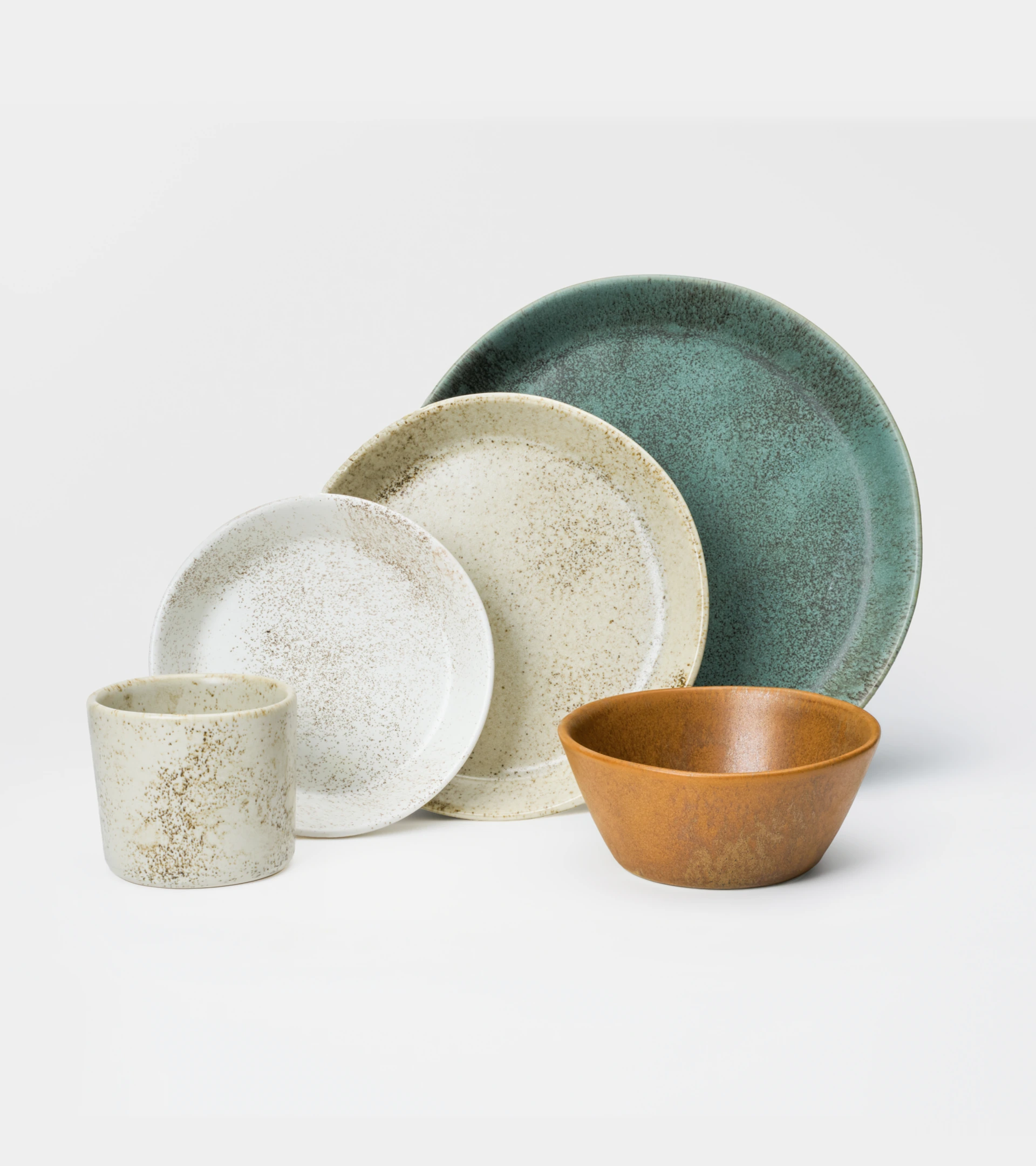 Product photography of a speckled stoneware dinnerware set with plates, a bowl and a cup