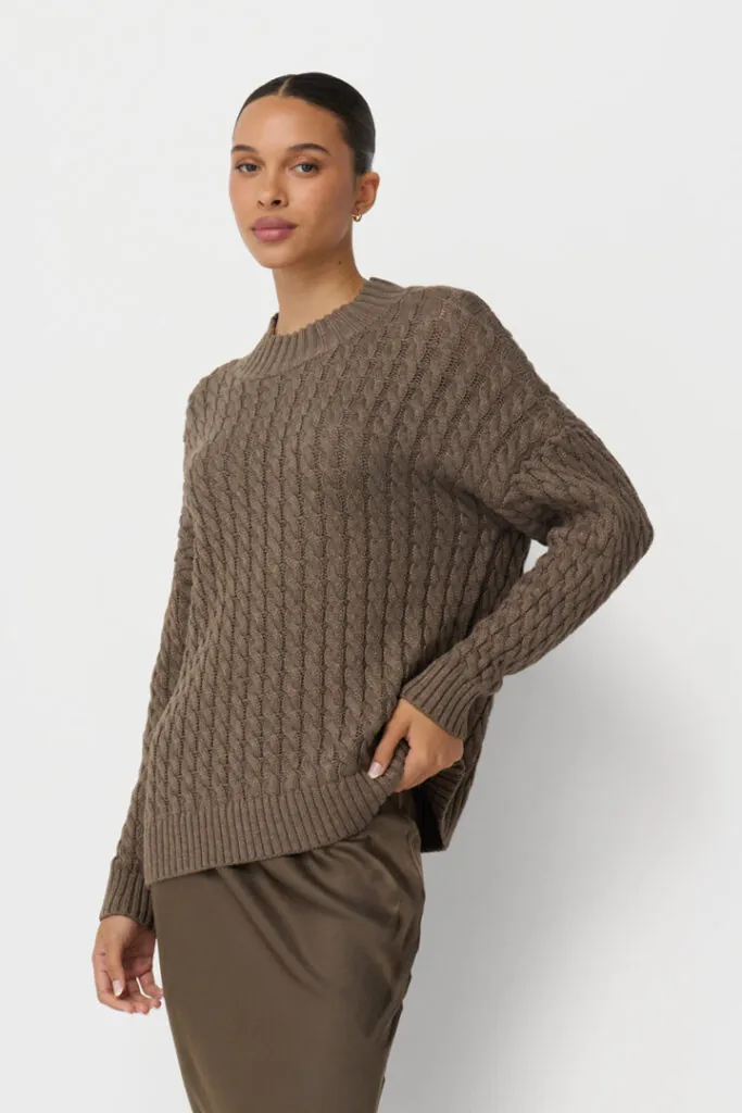 On-model photography of a taupe oversized blazer styled with a brown sweater tied over the shoulders, shown in a three-quarter crop