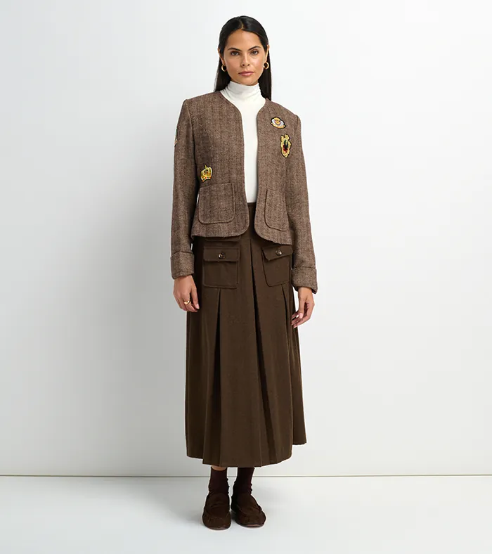 On-model photography of a brown tweed jacket with brooches, turtleneck, and pleated brown midi skirt