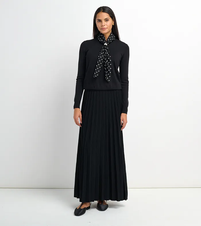 On-model photography of a black sweater with polka-dot neck scarf and pleated maxi skirt